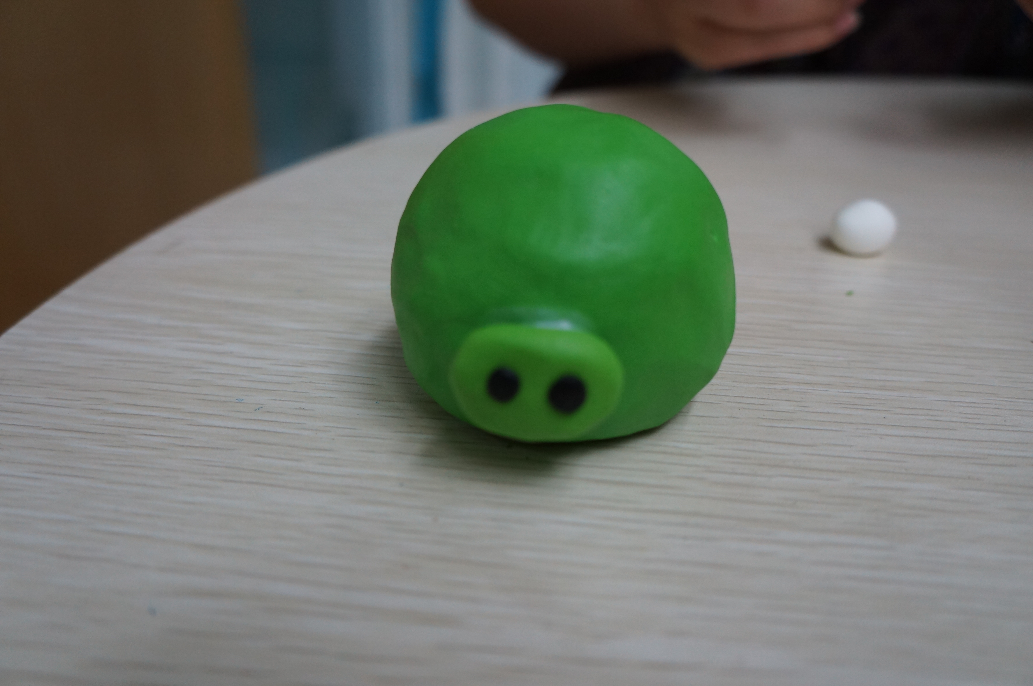 7,取一块深绿色黏土,分两半,揉圆,压扁,做成水滴状,粘在绿皮猪头上